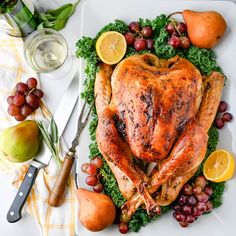 a roasted turkey on a platter surrounded by fruits and vegetables