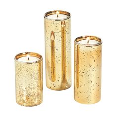 three gold colored candles sitting next to each other on a white surface with speckles