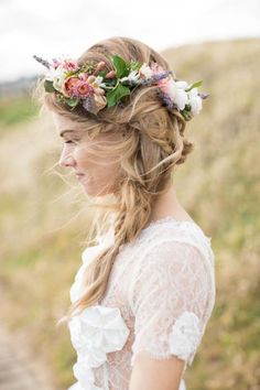 a woman with long hair wearing a flower crown on her head standing in the grass