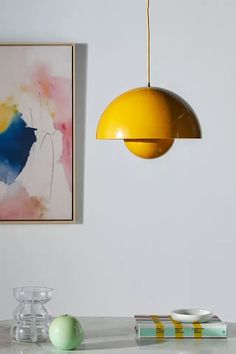 a yellow light hanging over a table next to a painting on the wall and vases