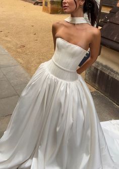 a woman in a white dress is standing on the sidewalk and looking off into the distance