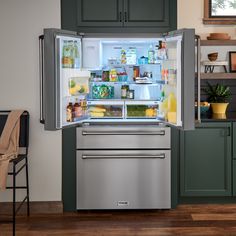 an open refrigerator with its door wide open in a kitchen, next to green cabinets