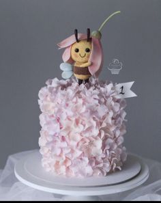 there is a small cake decorated with pink flowers and a bee on top of it