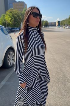 This stunning blue and white striped dress is made from polyviscose, featuring a half-turtleneck and a zip closure at the back. The dress has two asymmetrical ruffles and long sleeves with buttoned cuffs. Its unique and modern design is suitable for various body types, offering a loose fit that doesn't cling to the body, providing comfort and freedom of movement. The asymmetry and elegant style make this dress a fashionable choice for any occasion. Made of: Viscous Polyester This top can be cust Long Sleeve Dresses With Vertical Stripes For Work, Long Sleeve Vertical Stripes Work Dress, Long Sleeve Vertical Stripe Work Dresses, Chic Striped Mini Dress With Ruffles, Chic Long Sleeve Dresses With Vertical Stripes, Striped Long Sleeve Midi Dress For Work, Chic Striped Long Sleeve Midi Dress, Elegant Striped Long Sleeve Mini Dress, Flounces Dress