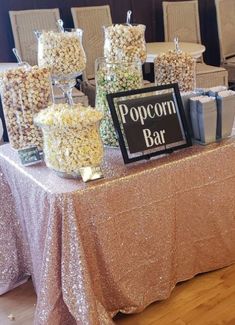 a table topped with lots of popcorn covered in glitter next to chairs and a sign that says popcorn bar