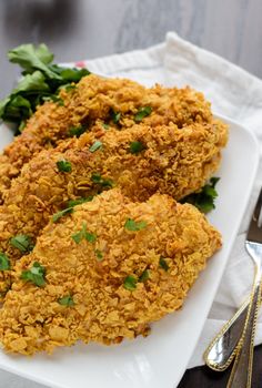 fried chicken on a white plate with parsley garnish and silverware next to it