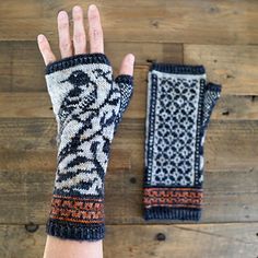 a woman's hand with two knitted mitts on top of a wooden table