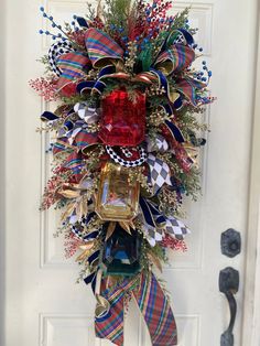 a christmas wreath hanging on the front door with red, white and blue ribbons around it