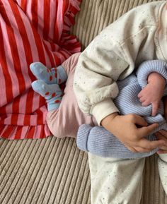 a baby laying on top of a couch next to a person holding a stuffed animal