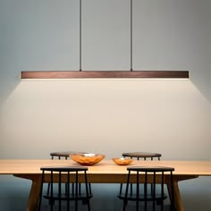 two bowls sit on top of a wooden table with four chairs around it in front of a white wall