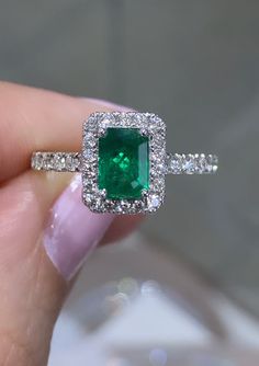 a woman's hand holding an emerald and diamond ring