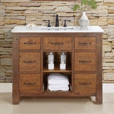 a bathroom vanity with wooden drawers and white towels on the counter top next to a stone wall