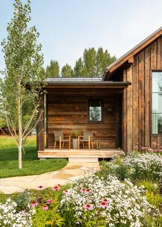 a wooden house with flowers in the foreground and an outdoor dining area on the other side