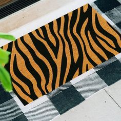 a close up of a door mat with a tiger pattern on it and a plant