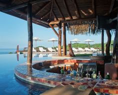 an outdoor bar next to the ocean with chairs and umbrellas on it's roof