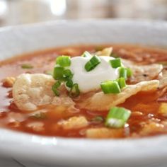 a close up of a bowl of soup with sour cream and green onion garnish