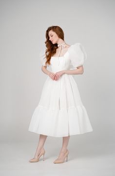 a woman is wearing a white dress with ruffles on the shoulders and heels