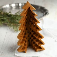 a small wooden christmas tree sitting on top of a white cloth covered table next to a metal pan