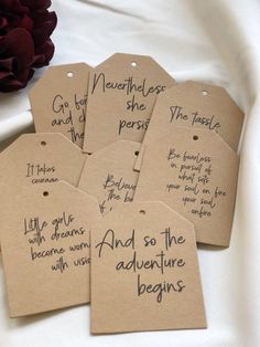 four tags with handwritten words on them sitting next to a red rose and white cloth