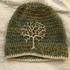 a green and white knitted hat with a tree on the front, sitting on top of a bed