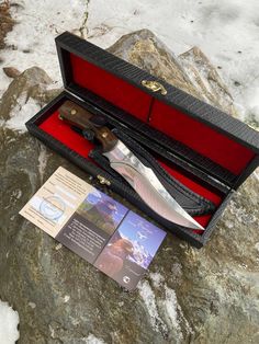 an open case with a knife in it sitting on top of some snow covered rocks