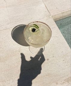 the shadow of a person standing next to a glass with a flower in it on concrete