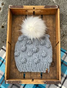 a knitted hat in a wooden box with a white pom - pom