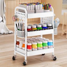 a white cart with lots of paint and supplies on it's wheels in a room