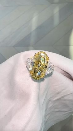 a fancy yellow diamond ring sitting on top of a white gloved hand in front of a wall