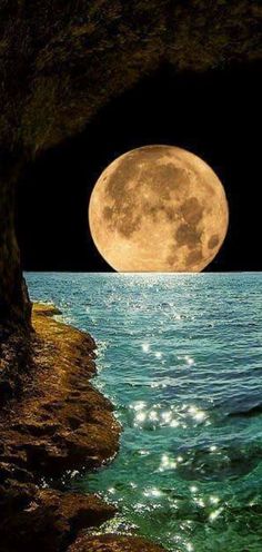 a full moon is seen over the ocean with rocks and water in front of it