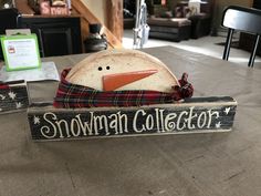 a wooden snowman decoration sitting on top of a table next to a sign that says snowman collector