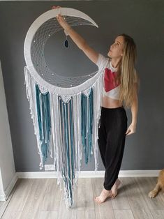 a woman standing in front of a white and blue dream catcher on the floor next to a dog