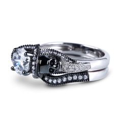 Each of our skull ring is unique and special, just like the love of your life. Crafted in sterling silver, the ring features a shimmering round cut center stone wrapped in a frame of smaller round stones and flanked by two black skull heads. The coordinating contoured band fits closely with the engagement ring, completing this stunning design. Skulls represent freedom, individuality and a celebration of rebirth. This perfect skull ring set seals your vows with stunning style.Carat Weight: 2.5 ctStone Size: 7 mmStone Type: Jeulia® StoneNumber of Stones: 1 Stone Color: Diamond WhiteStone Shape: RoundCarat Weight: 1.166 ctStone Size: 2.5,1.5,1.3,1.25,1.2,1.1,1 mmStone Type: Jeulia® StoneNumber of Stones: 87 Stone Color: Diamond WhiteStone Shape: RoundWeight: 7.27 gWidth: 9.31 mmHeight: 7.07 m Skull Shaped Sterling Silver Ring In White Gold, White Gold Skull Jewelry For Promise Ring, Adjustable Round Skull Ring For Anniversary, Adjustable Skull Ring For Anniversary, White Gold Skull Ring As A Gift, Sterling Silver Skull Ring For Wedding, White Gold Skull Ring For Gift, White Gold Skull Rings As Gift, Sterling Silver Skull Ring For Anniversary