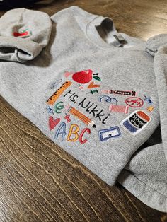 a child's hoodie with embroidered letters and symbols on the front, sitting on a wooden surface