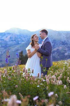 a bride and groom standing in the middle of a field with mountains in the background