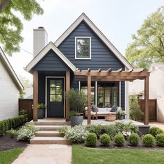 a small blue house with a porch and pergolated area in the front yard