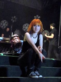 a woman with red hair is sitting on the steps in front of a drum set