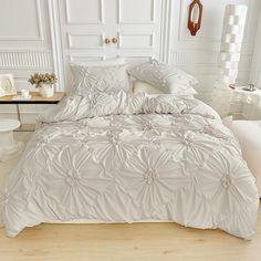 a bed with white comforter and pillows in a room next to a table on the floor