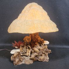 a mushroom lamp is sitting on top of some rocks and dirt, with an oak stump underneath it