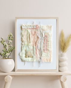 a white vase sitting on top of a wooden shelf next to a framed art piece