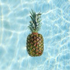 a pineapple floating on top of a blue swimming pool with water ripples around it