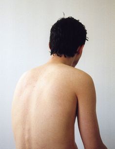 the back of a man with no shirt on is standing in front of a white wall