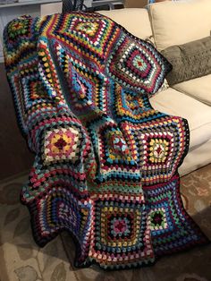 a crocheted granny blanket sitting on top of a couch next to a pillow