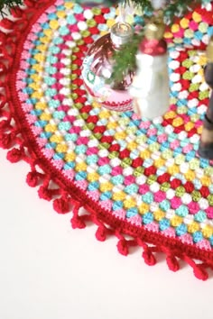 a crocheted table mat with ornaments on it and a christmas tree in the background