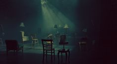 an empty room with chairs and lamps on the floor, in front of a dark background