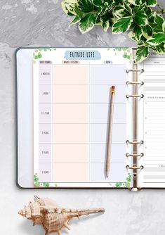 an open planner with a pen and plant on the table next to it, along with a seashell