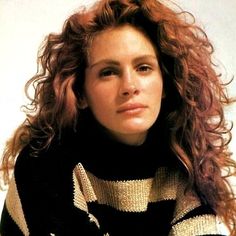 a woman with long curly hair wearing a black and white striped sweater looking at the camera