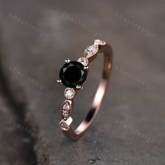 a black diamond ring sitting on top of a gray stone surface with diamonds around it