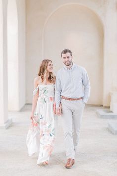 an engaged couple holding hands and walking in front of arches