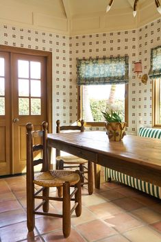 a wooden table sitting in front of a window next to a bench and chair on top of a tiled floor